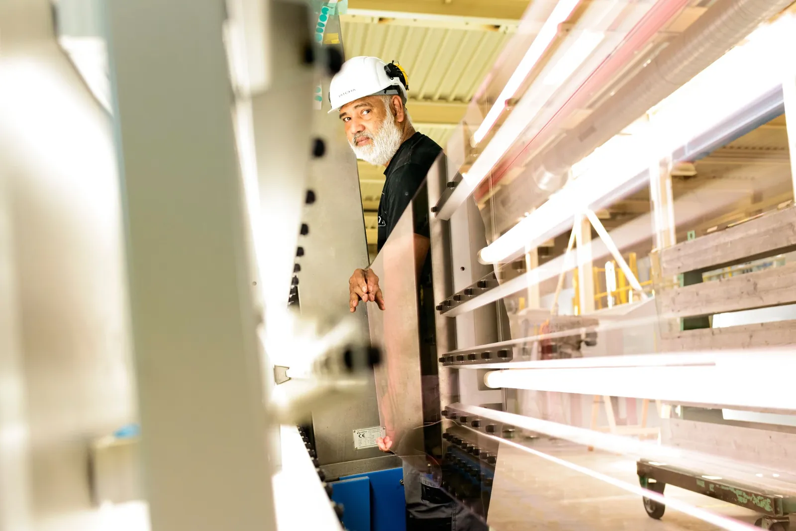 Mitarbeiter mit Schutzhelm führt eine Glasscheibe an der senkrechten Kantenmaschine